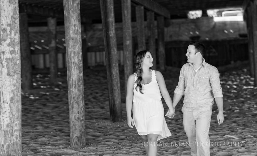 couple walking under the boardwalk at long branch beach engagement