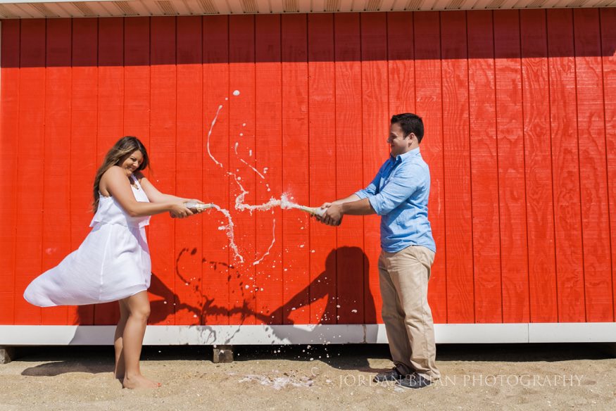 couple having champagne fight on beach at McLoone's Pier House Engagement session