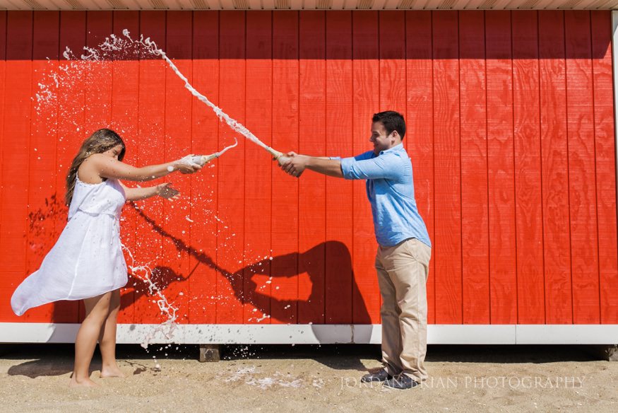 couple having champagne fight on beach at long branch beach engagement
