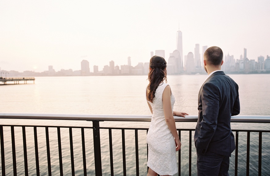 Elina and Thomas embracing with the NYC skyline glowing orange and pink behind them.