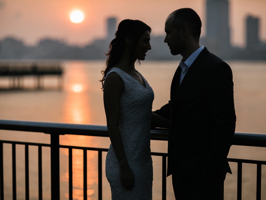 Elina and Thomas close together, Freedom Tower reflected in the Hudson River at dawn.