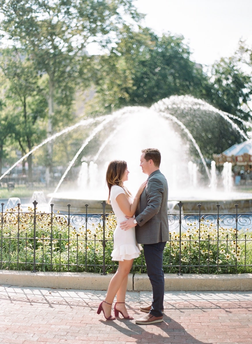 Vertical portrait of Jamie and Chad by the Franklin Square fountain with warm afternoon light.