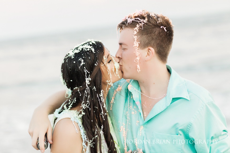 Couple spray eachother with silly string at Wildwood Engagement session.