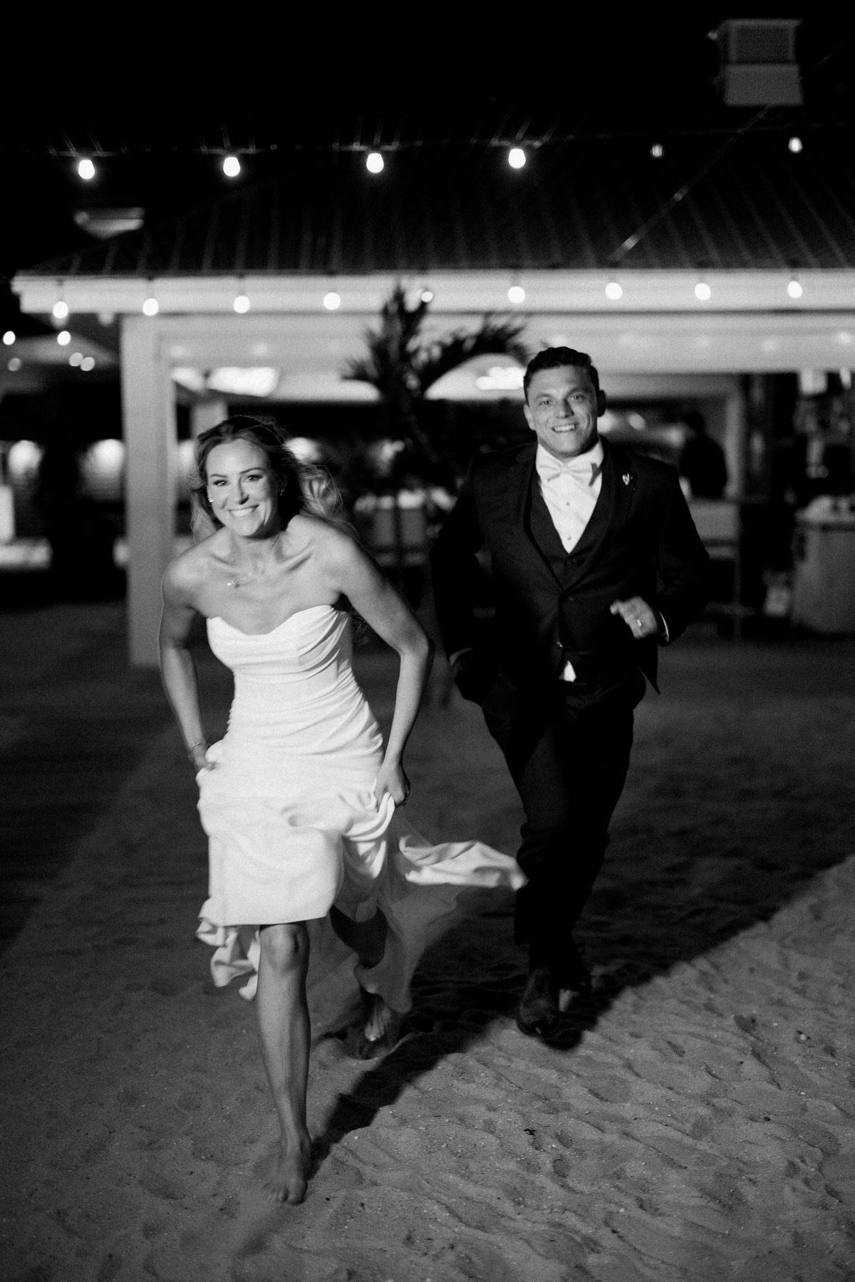 Night portrait of couple outside at ICONA Avalon with string lights and lit building in Avalon NJ