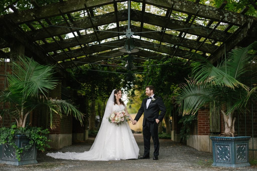 Bride and groom on their wedding day beneath the conservatory arbor at Grounds for Sculpture, Hamilton NJ