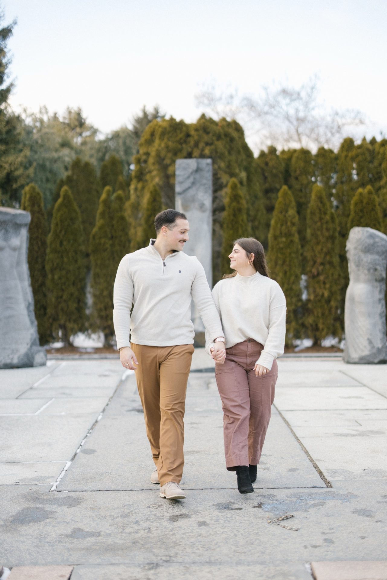 Newly engaged couple walking hand in hand through snowy Grounds for Sculpture garden Hamilton NJ engagement session