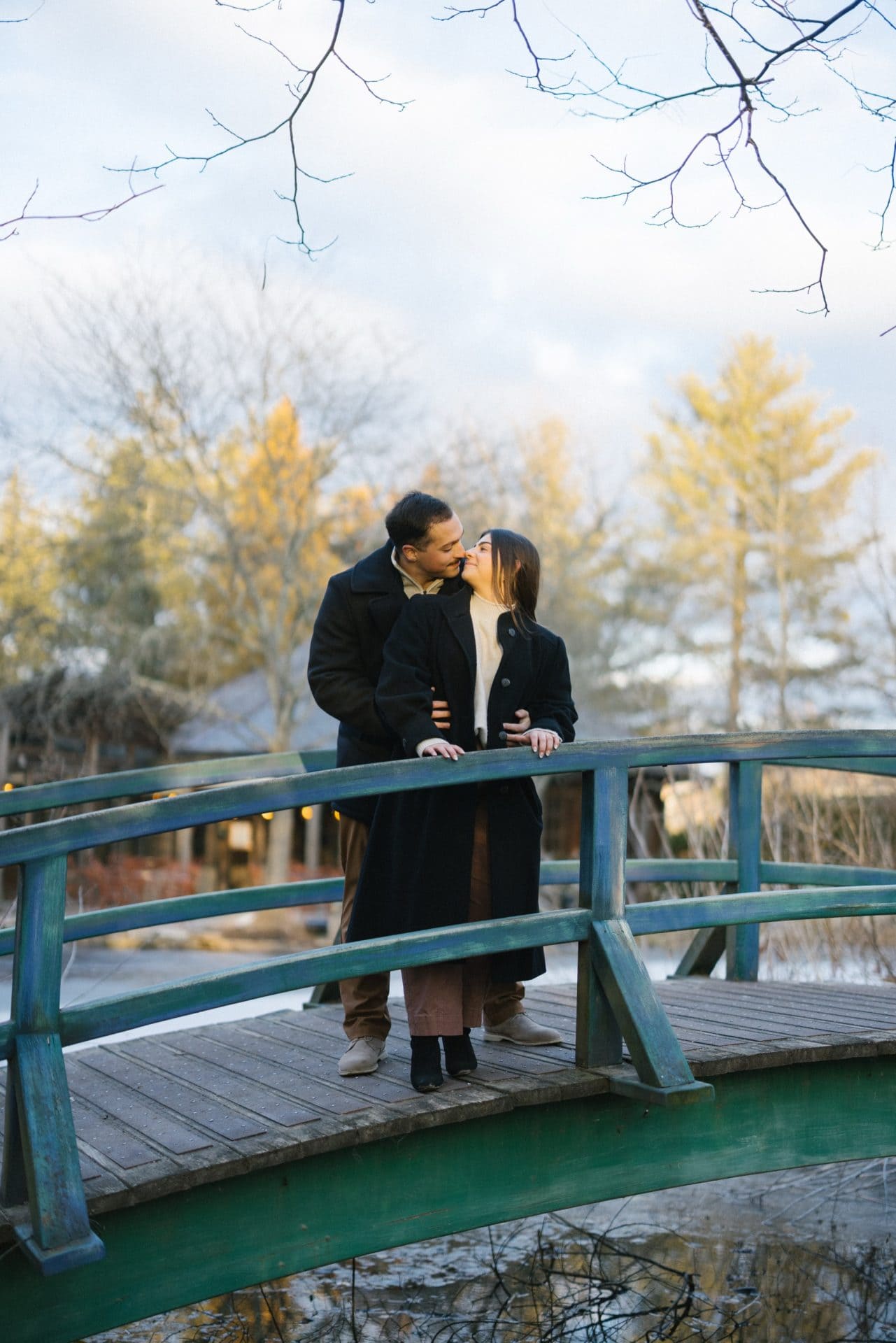 Couple kissing on bridge at Grounds for Sculpture after winter snow proposal Hamilton NJ engagement session