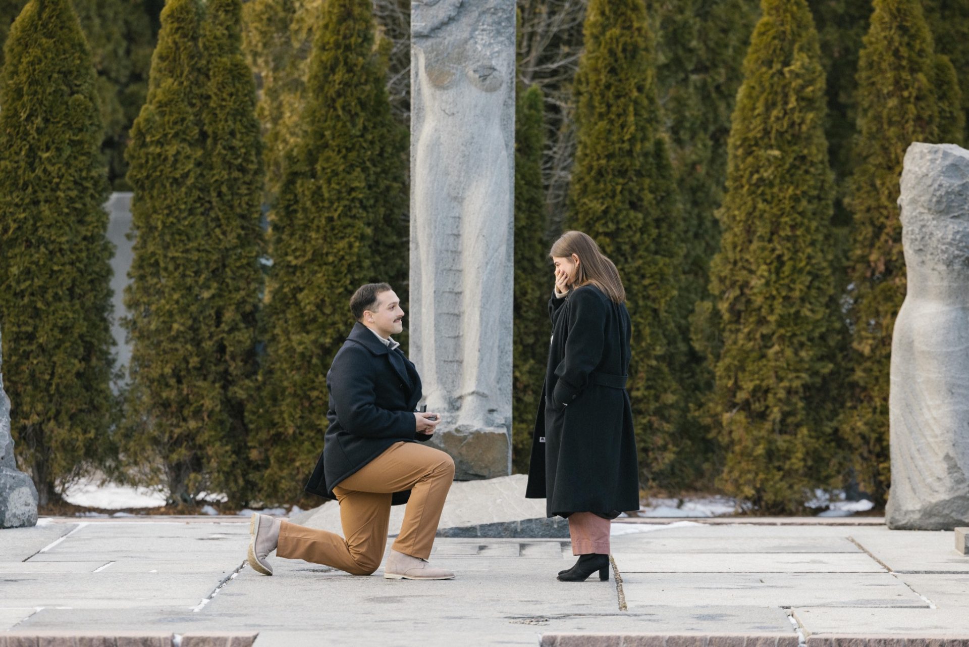 Surprise proposal moment at Nine Muses Grounds for Sculpture - she covers her face in shock during winter snow proposal Hamilton NJ