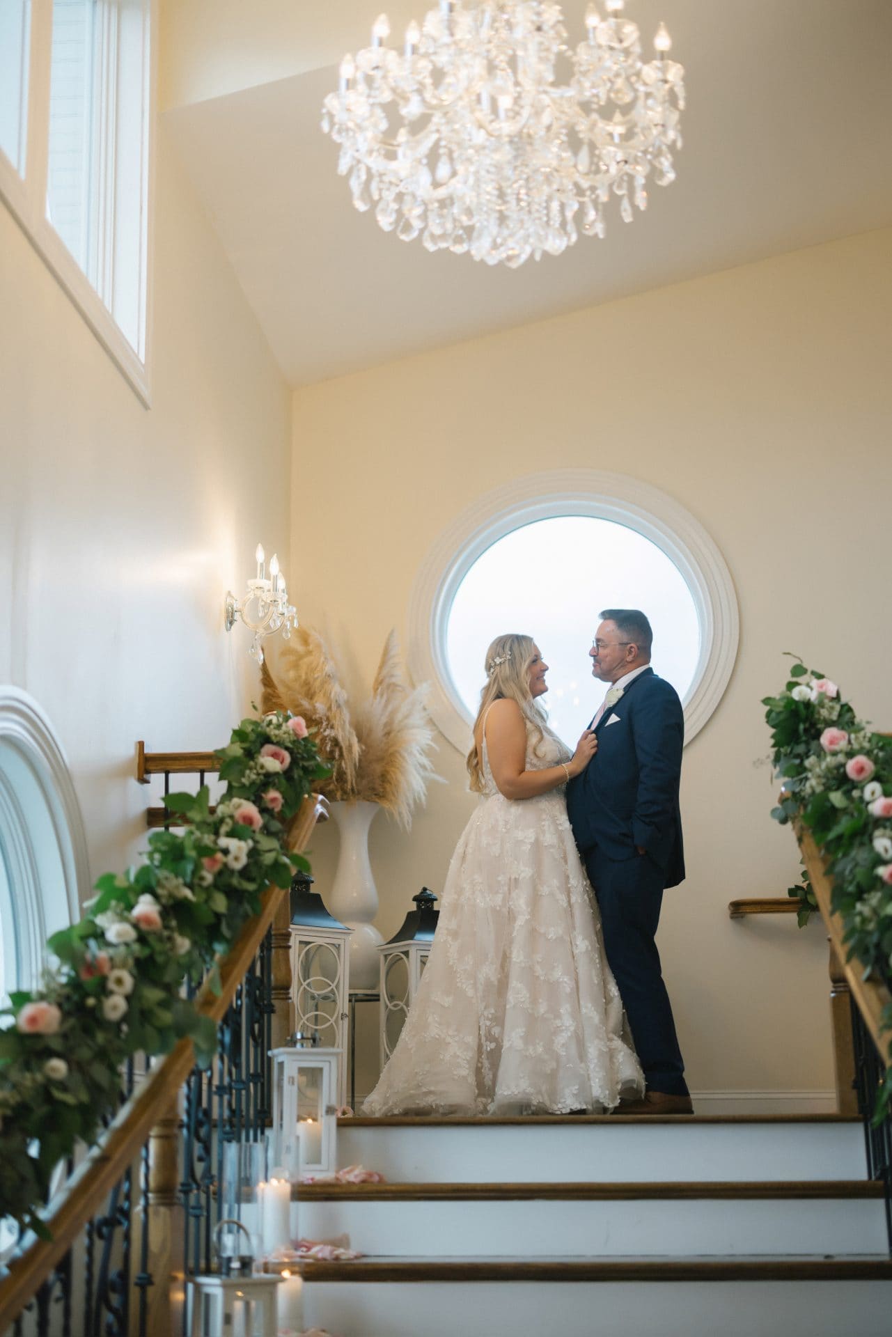 Couple on the stairwell with florals on the handrails and round window at Windows on the Water wedding, Sea Bright NJ