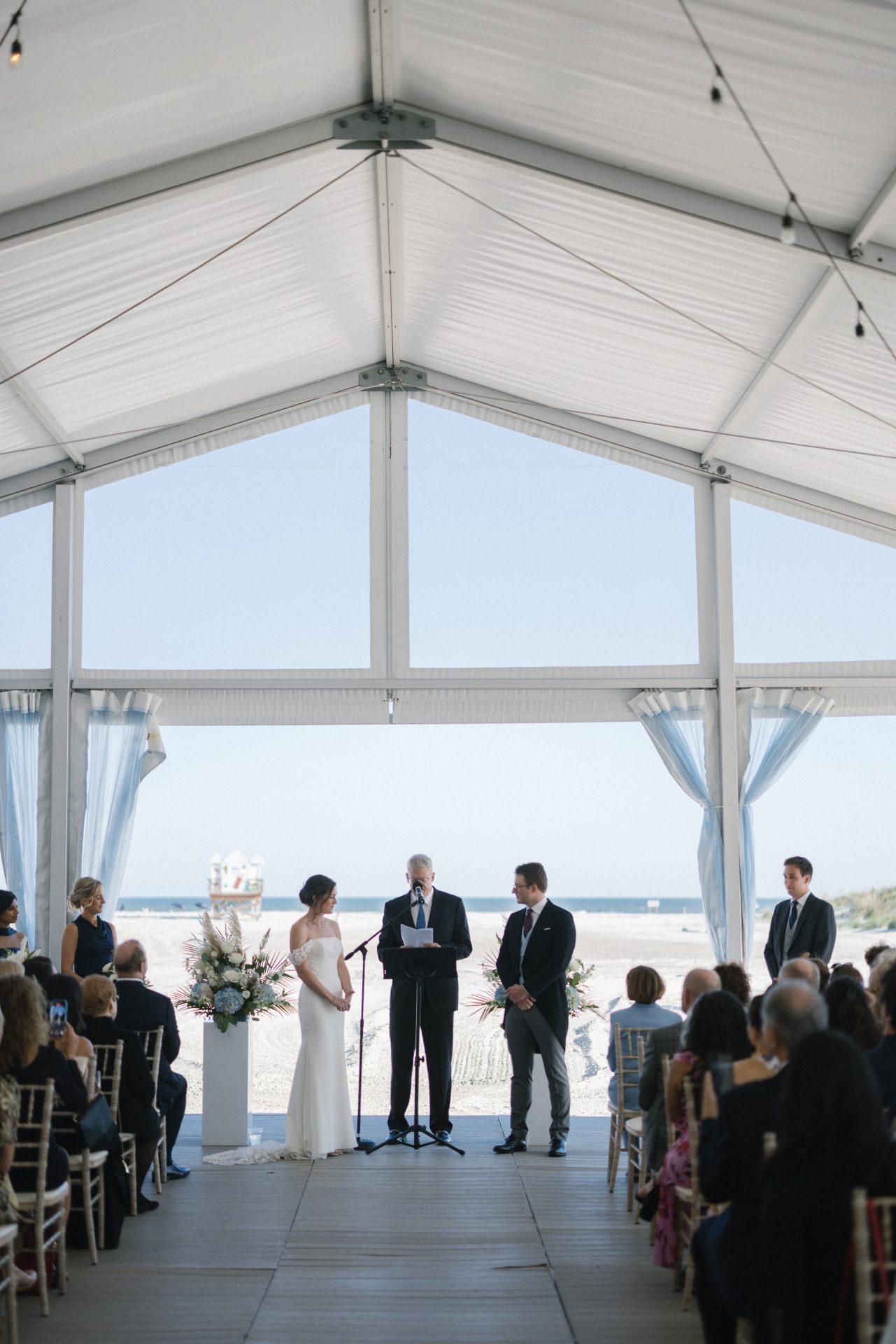 Beach tent ceremony with couple at altar and ocean visible through the glass panels at ICONA Diamond Beach Wildwood NJ