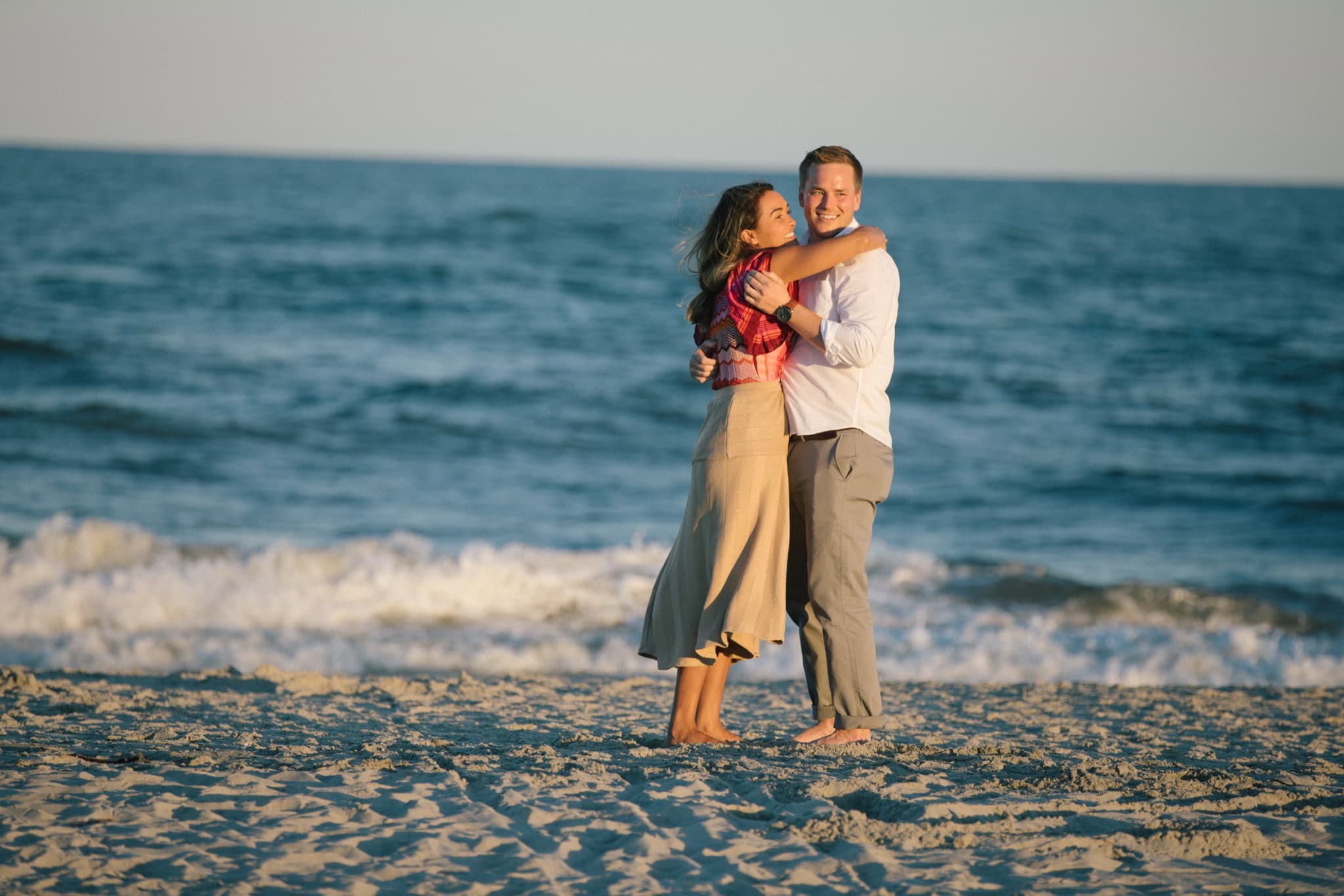 Newly engaged couple embracing on Sea Isle City beach after surprise proposal at golden hour