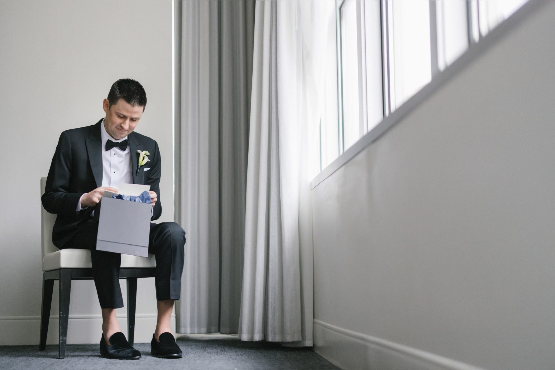 Groom opening gift box by hotel window on wedding morning at Loews Philadelphia