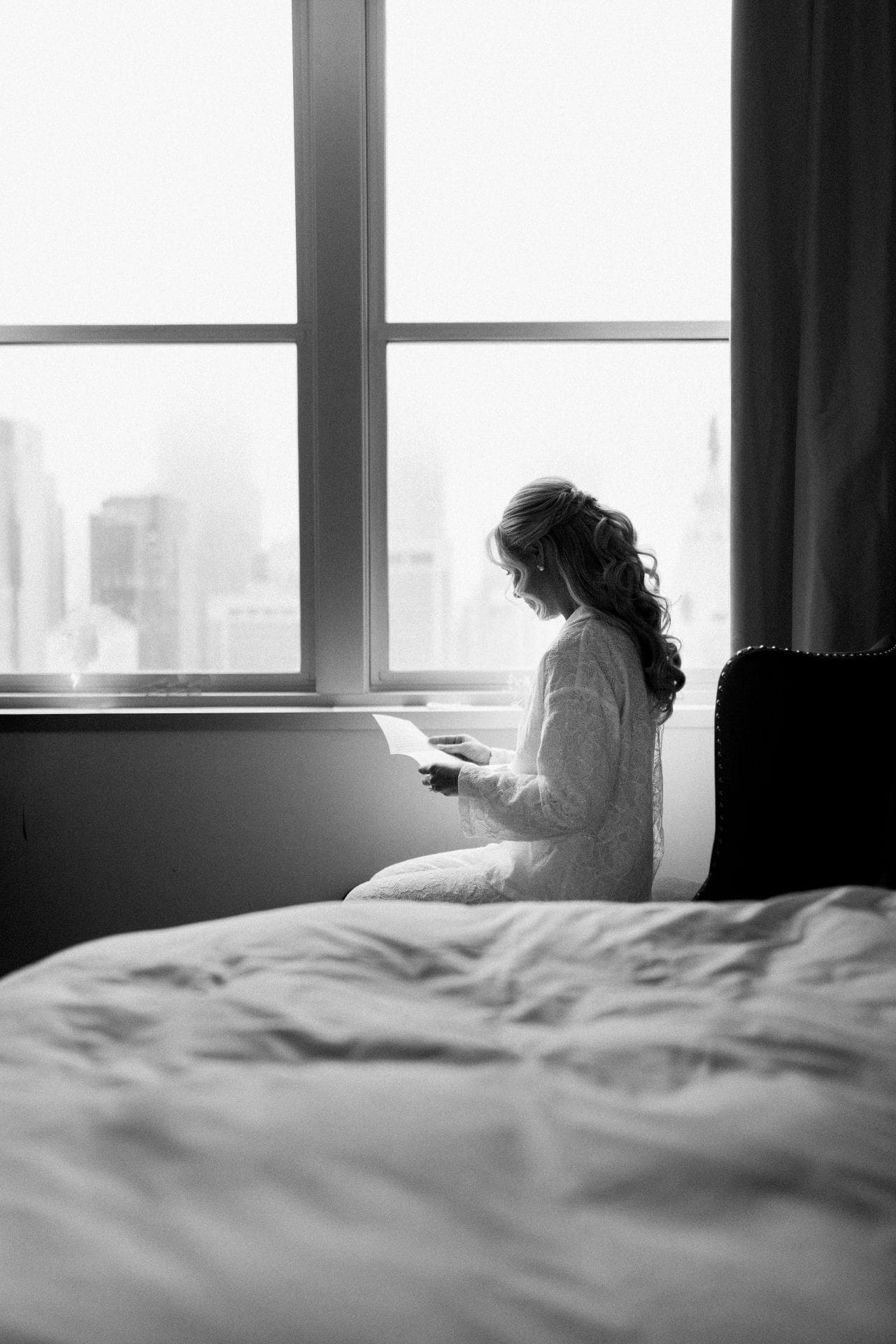 Bride reading letter from groom by window with Philadelphia skyline view