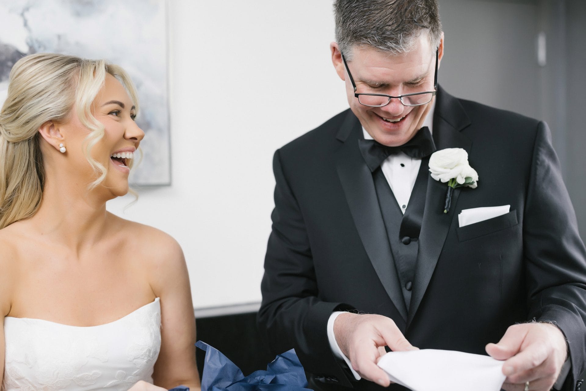 Bride laughing with father while he reads gift from daughter on wedding morning