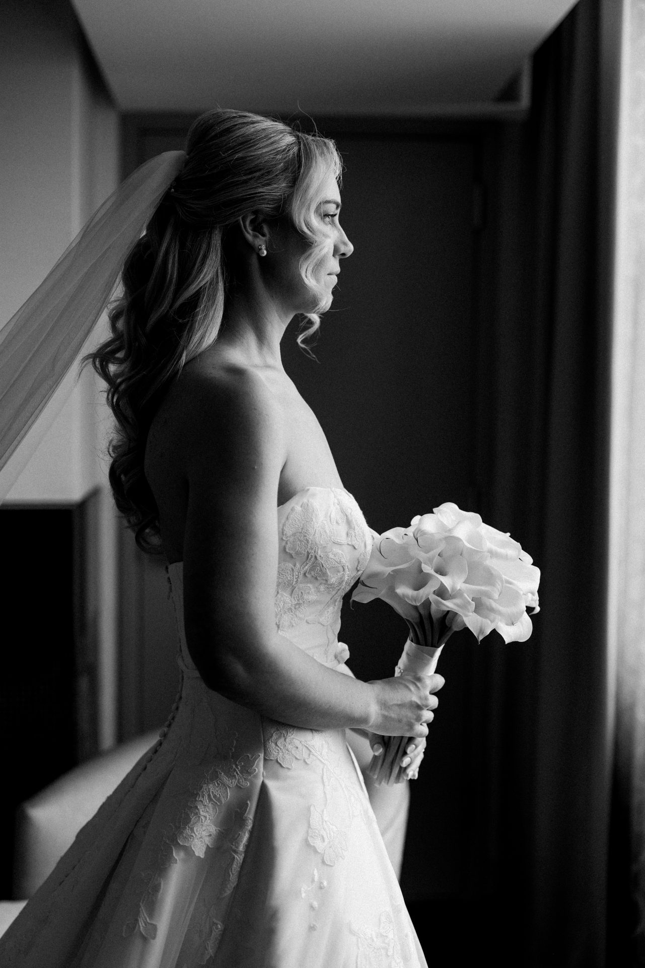 Dramatic bridal portrait by window holding calla lily bouquet in black and white