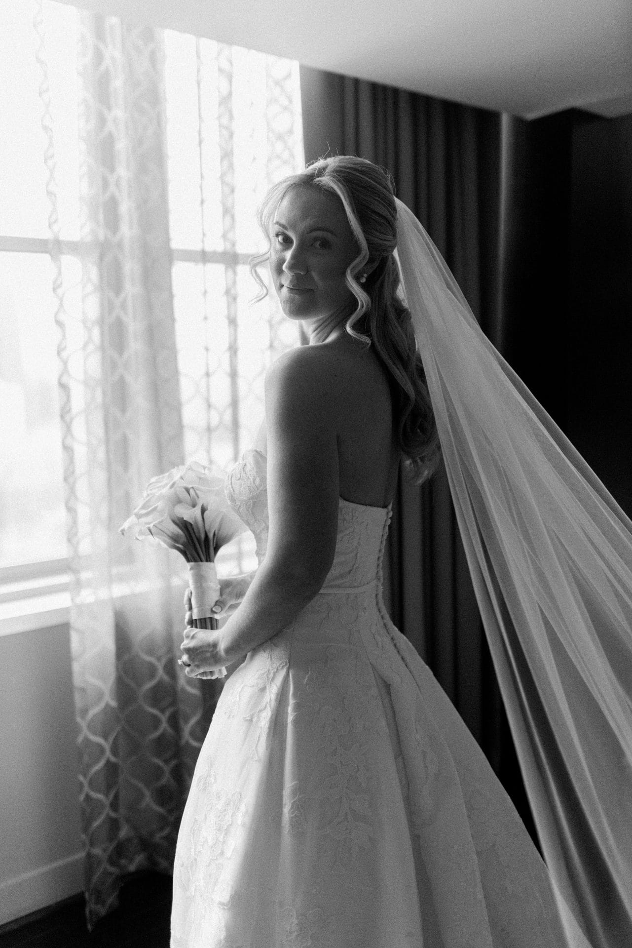 Bride looking over shoulder by window with veil flowing at Loews Hotel