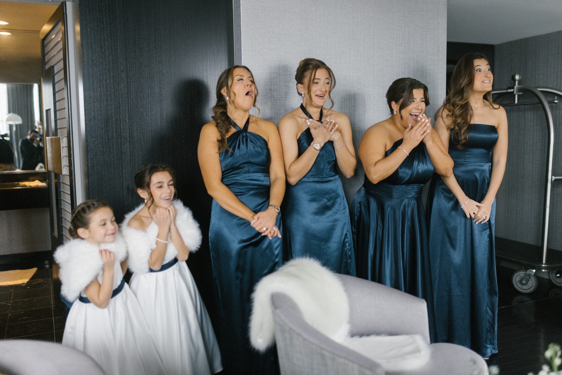 Bridesmaids in navy dresses and flower girls reacting to seeing bride for first time