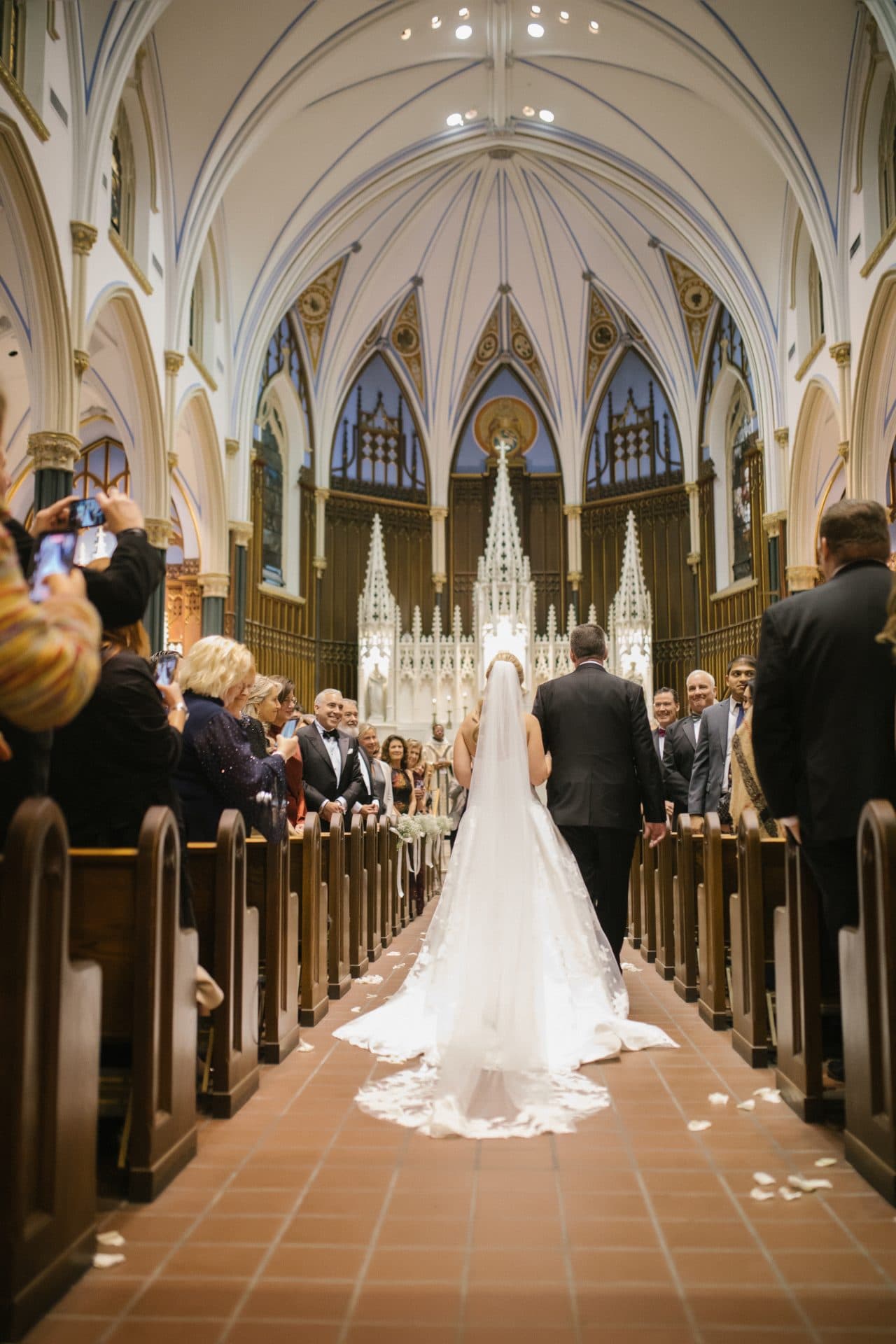 Bride and father walking down aisle with cathedral veil trailing at Philadelphia Catholic church