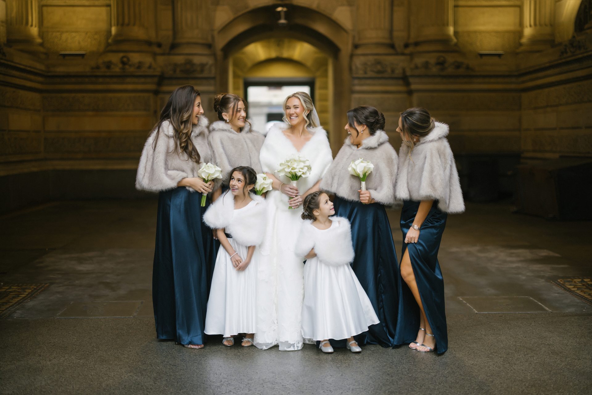 Bridesmaids in navy dresses with fur wraps laughing at City Hall Philadelphia