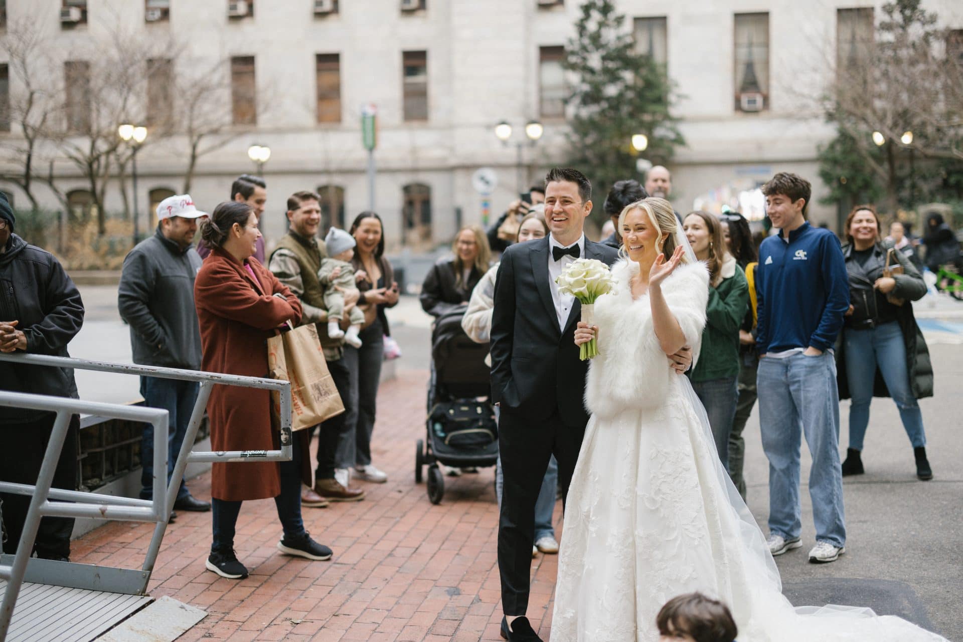Bride and groom walking on Broad Street Philadelphia while bystanders smile and watch