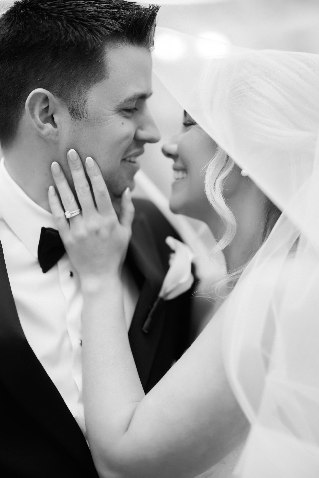 Intimate close up under veil bride hand on grooms face showing wedding ring