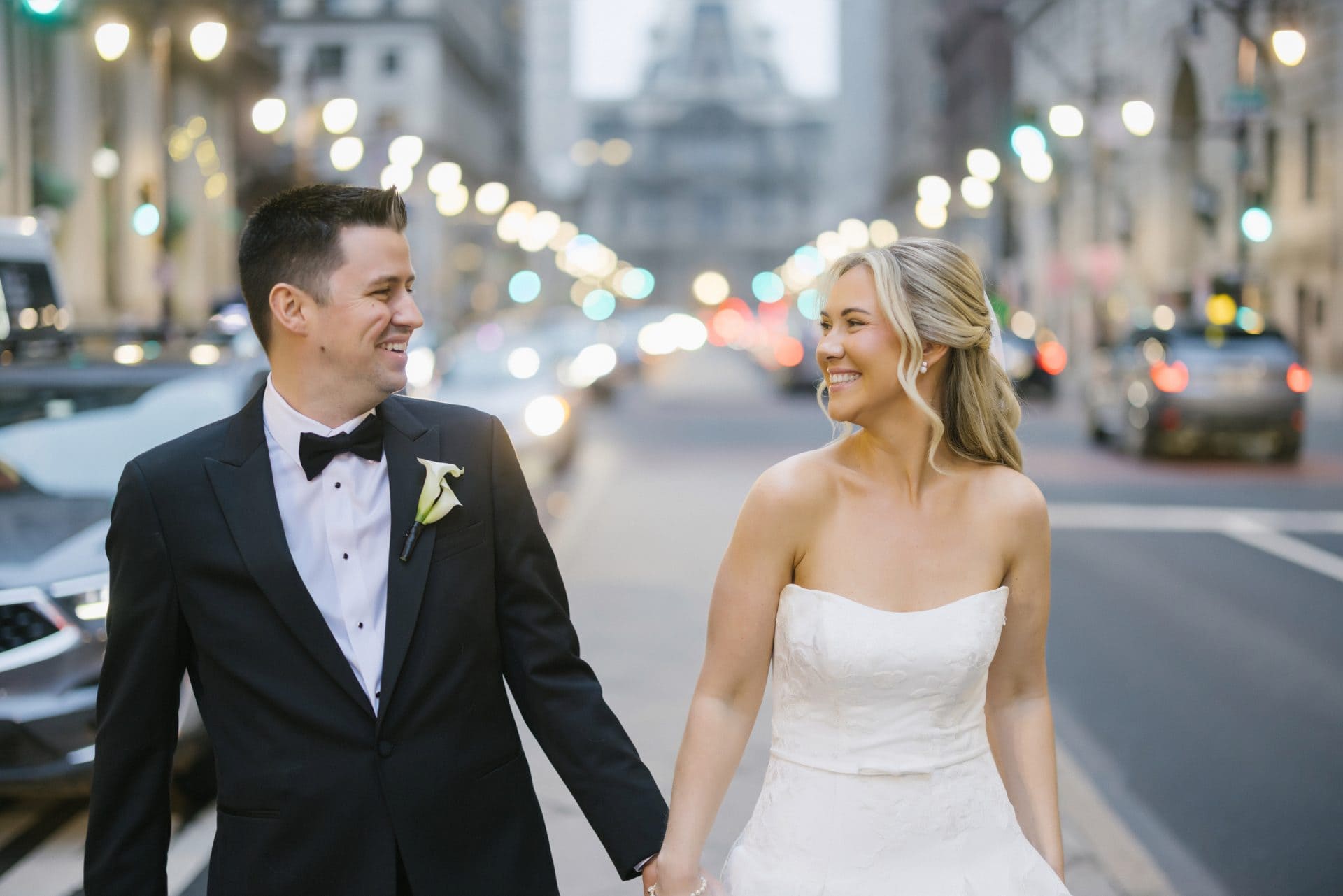 Couple walking hand in hand on Broad Street Philadelphia city lights behind them