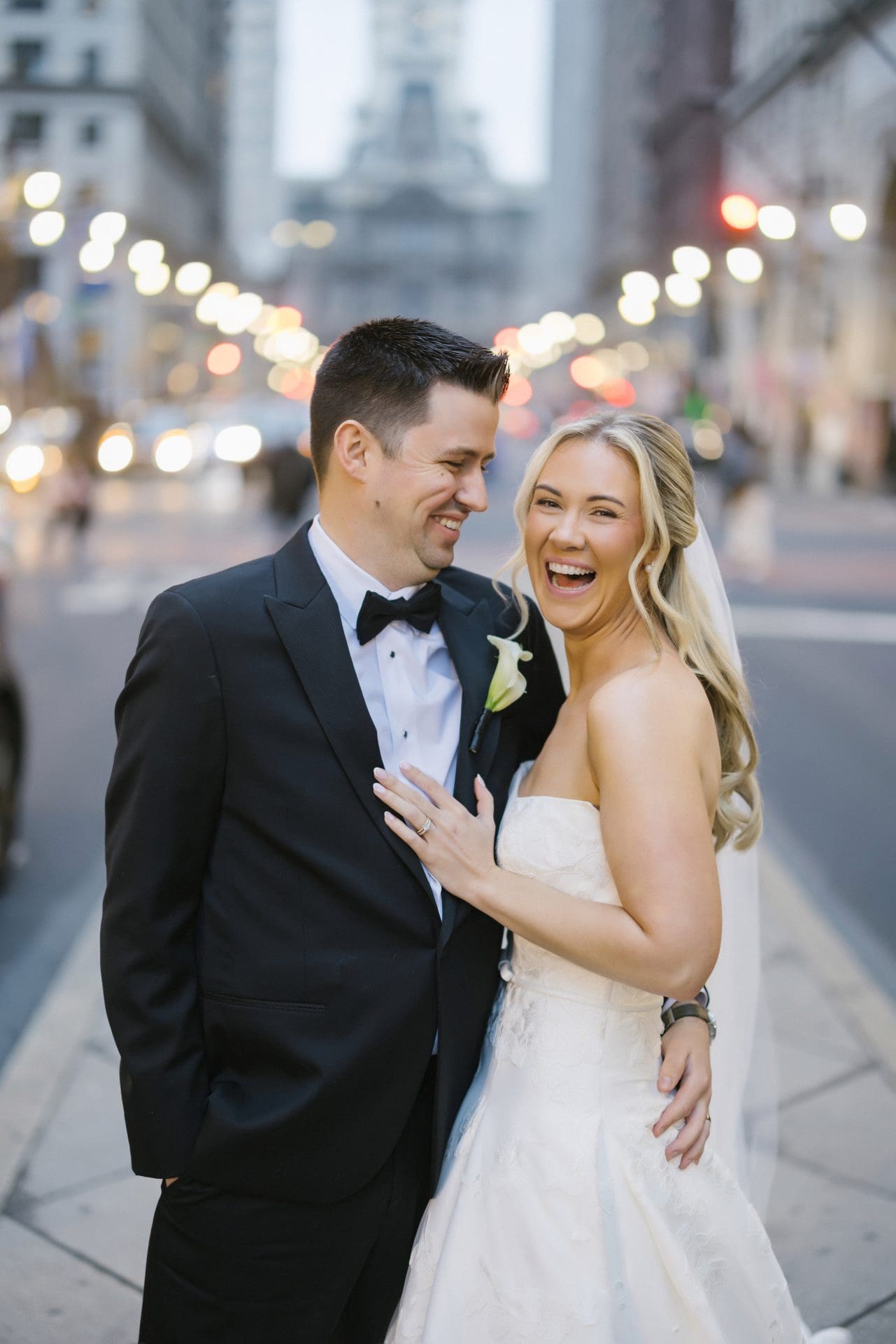 Bride and groom laughing on Broad Street with City Hall in background evening