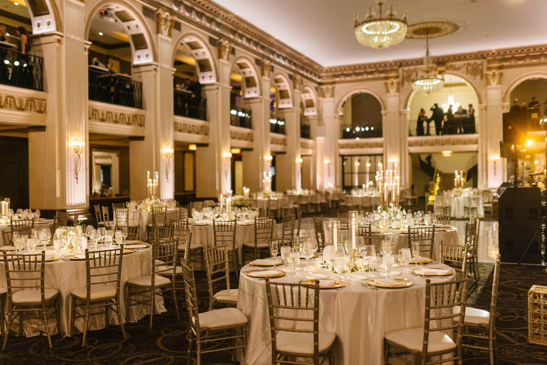 Wide shot Ballroom at the Ben reception room with round tables gold chairs grand arched columns