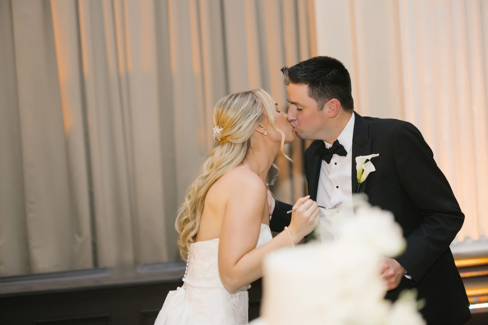 Couple kissing during cake cutting at Ballroom at the Ben wedding reception
