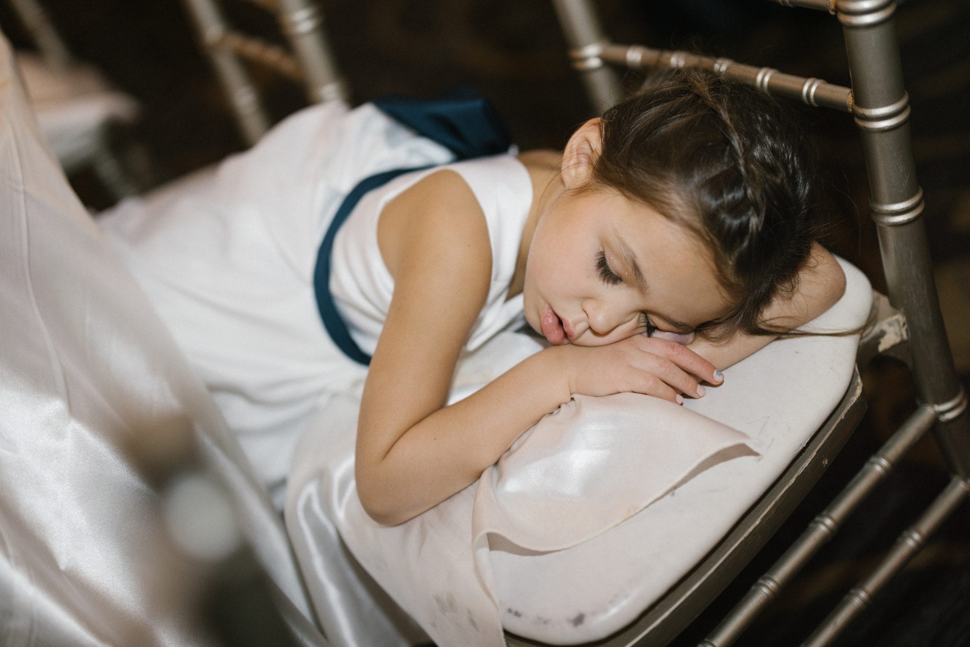 Flower girl asleep on chair sweet end of night moment at wedding reception