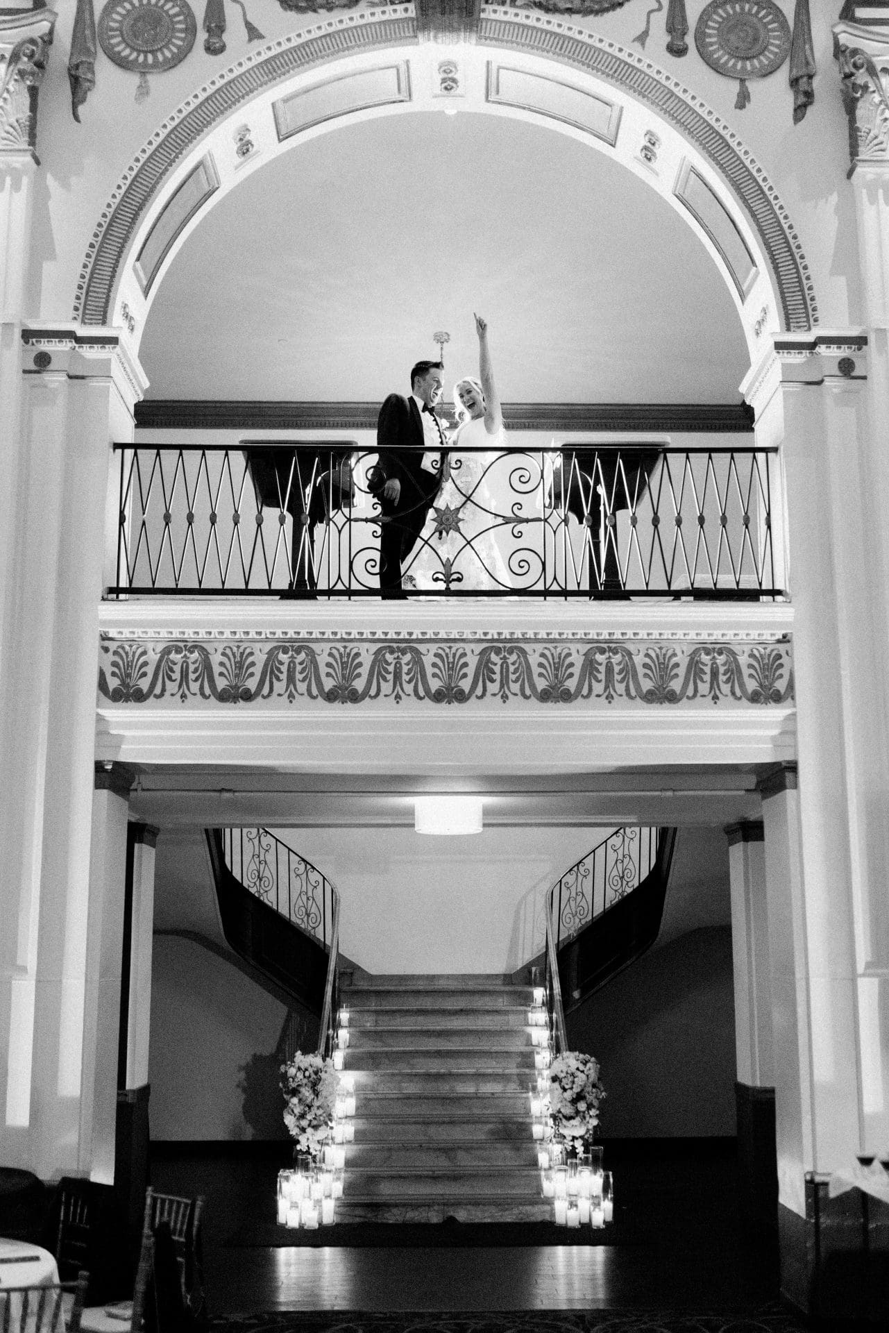 Couple on mezzanine balcony overlooking grand staircase lined with candles at Ballroom at the Ben