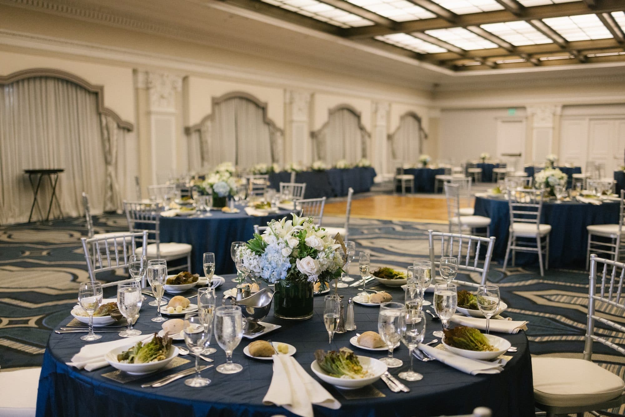 Reception table set with navy linens and gold chairs in the ballroom at The Notary Hotel