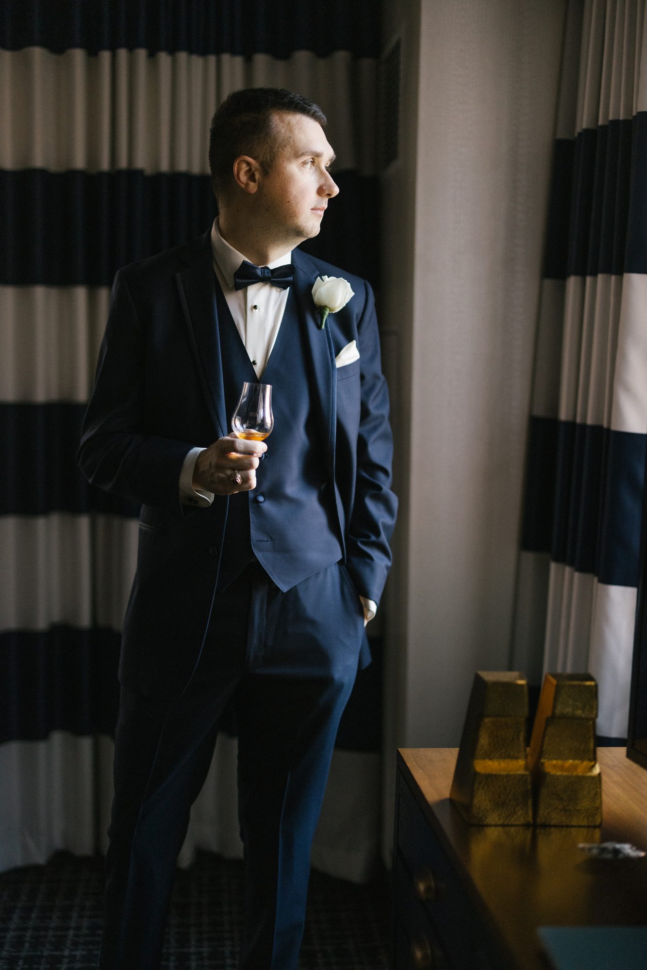 Groom in a tuxedo photographed in window light in a suite at The Notary Hotel