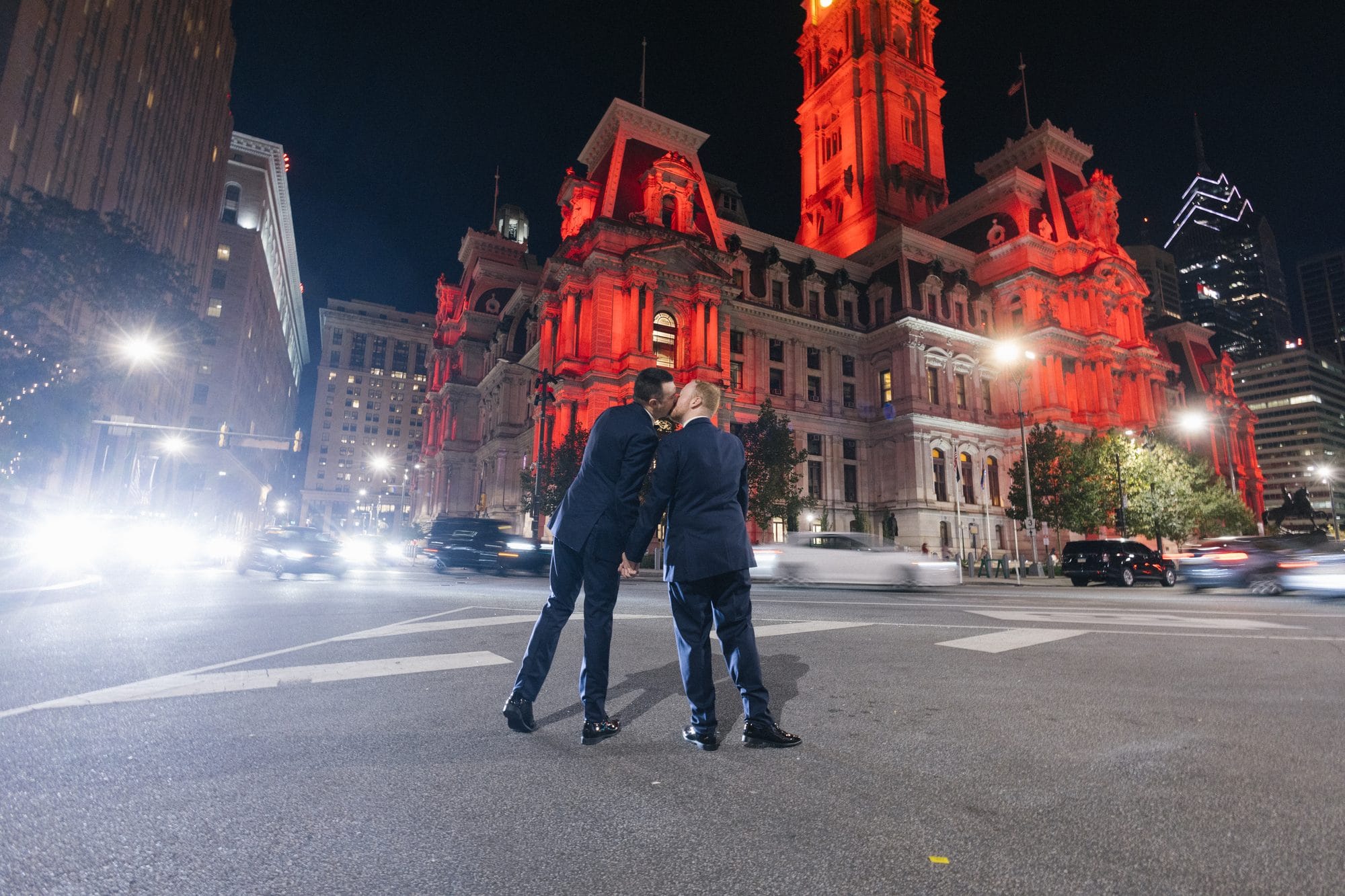 Couple standing in the street with Philadelphia City Hall lit red at night behind them