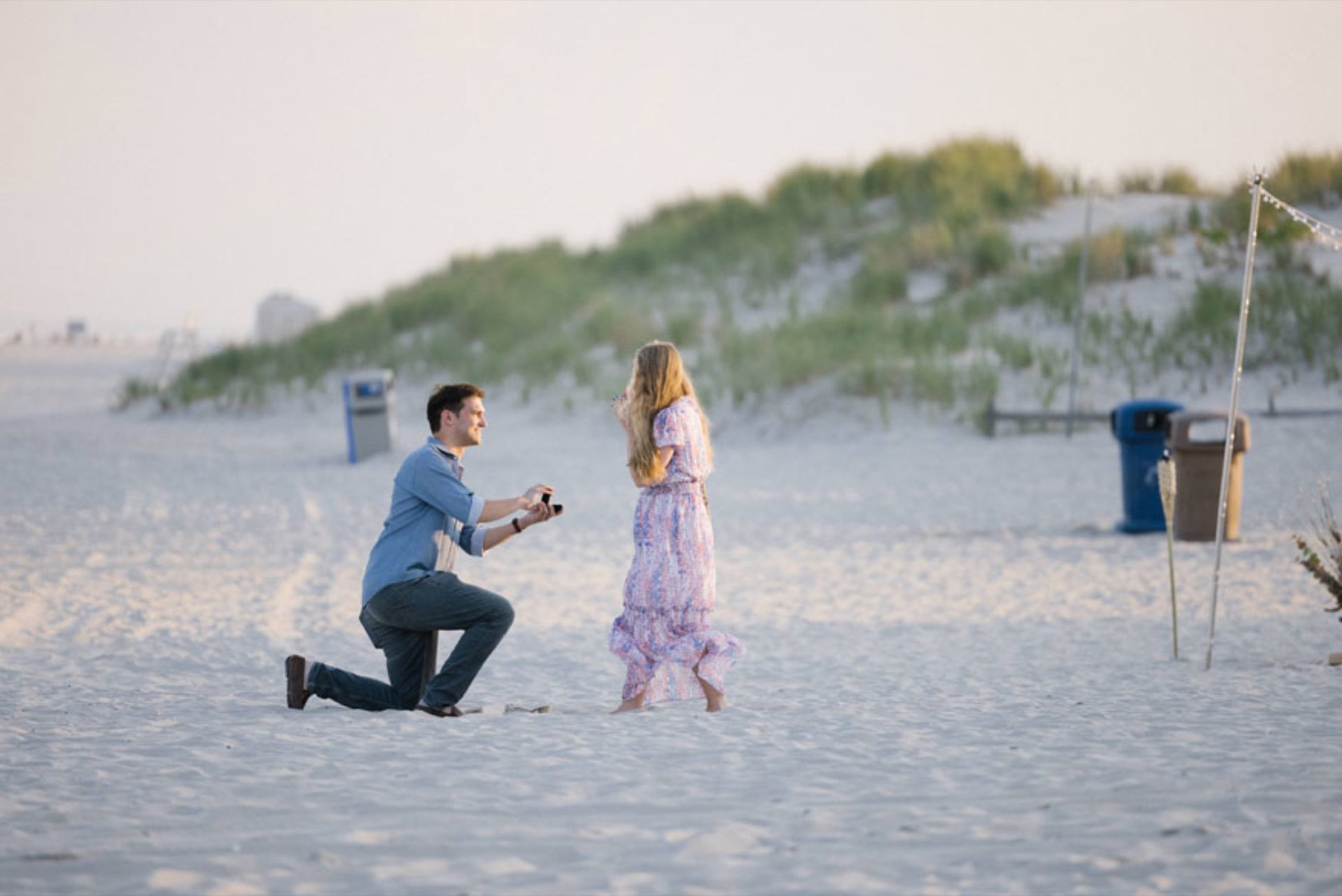 Couple embracing after surprise beach proposal at ICONA Avalon with ocean sunset in the background