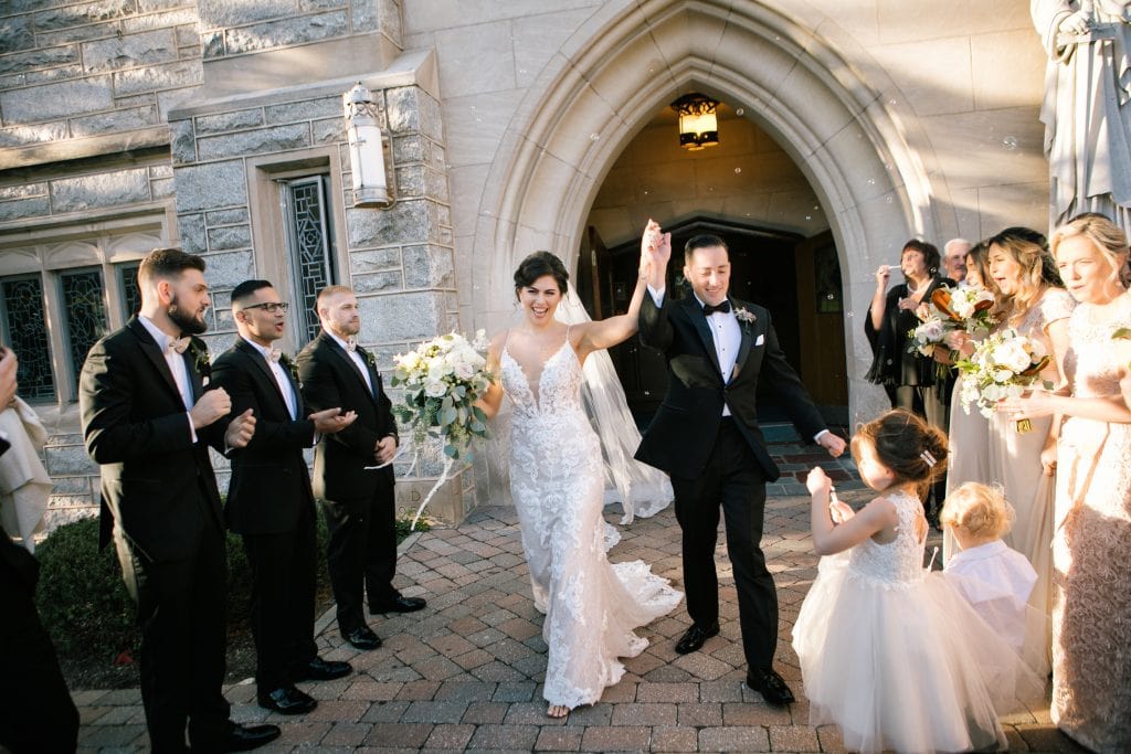 Bride and groom raise joined hands as they walk out of the church after their ceremony