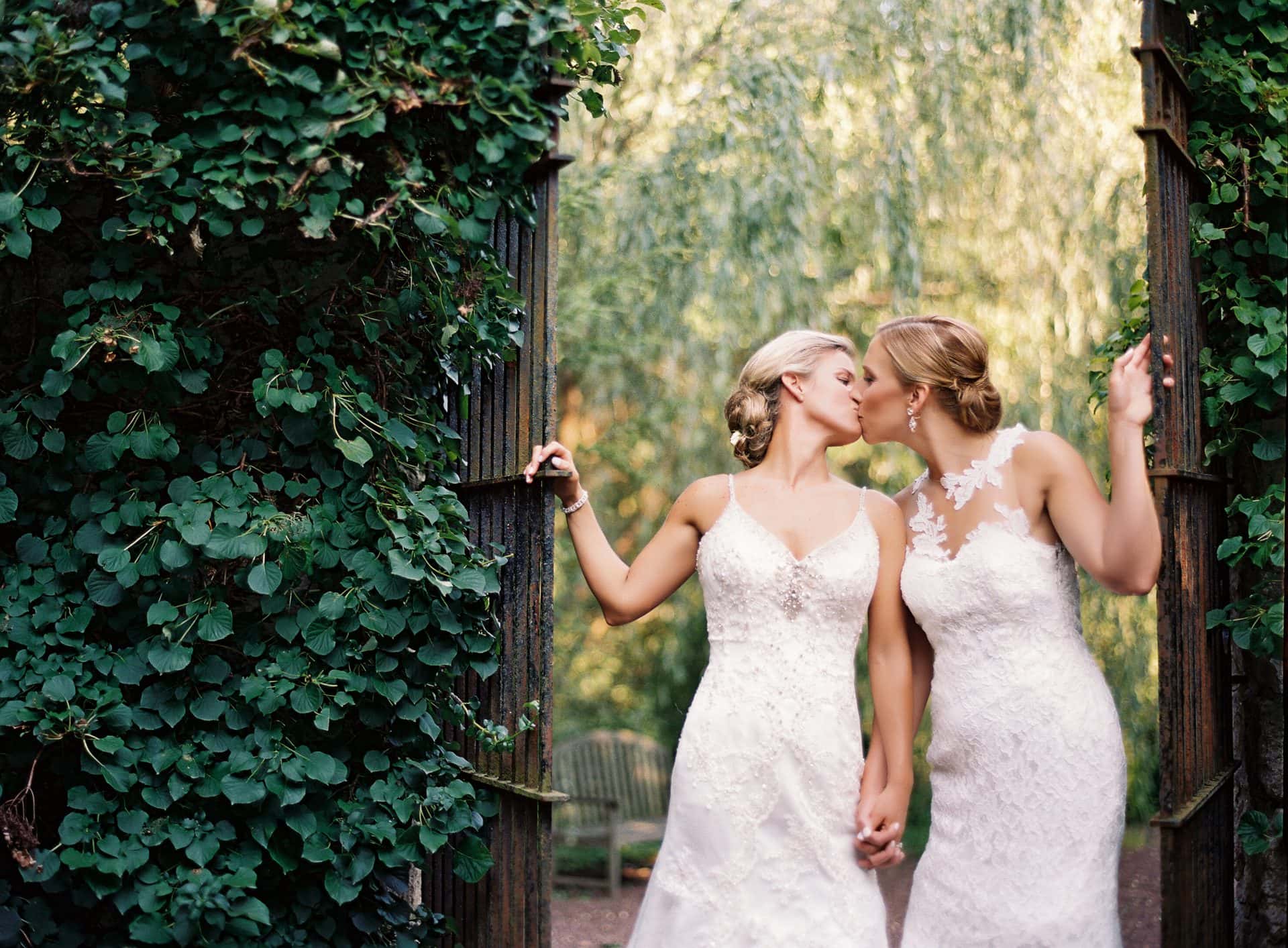 Two brides kissing at an ivy-covered garden gate, South Jersey wedding photography