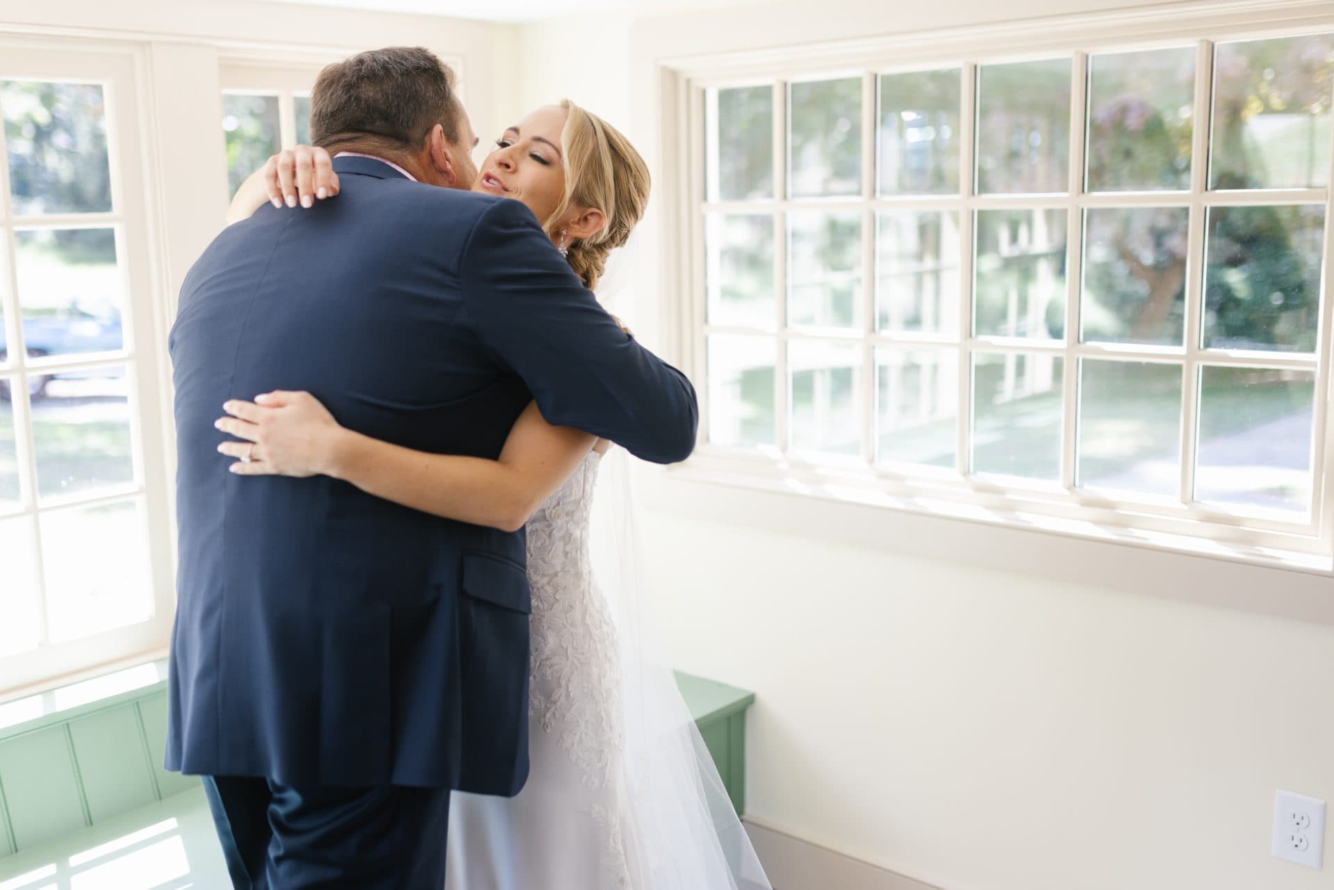 Bride and groom holding each other by a wall of bright windows, photographed by a Mount Laurel, NJ wedding photographer