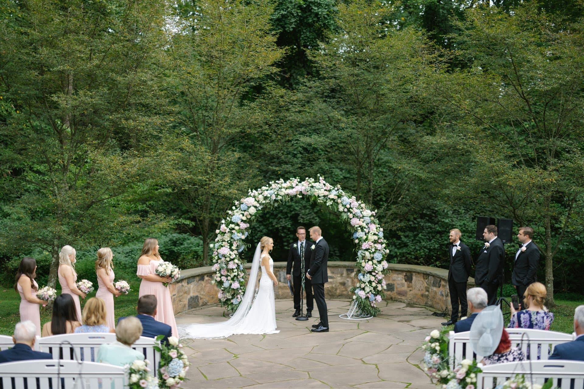 Outdoor ceremony under a floral arch on a stone terrace, by a Mount Laurel, NJ wedding photographer