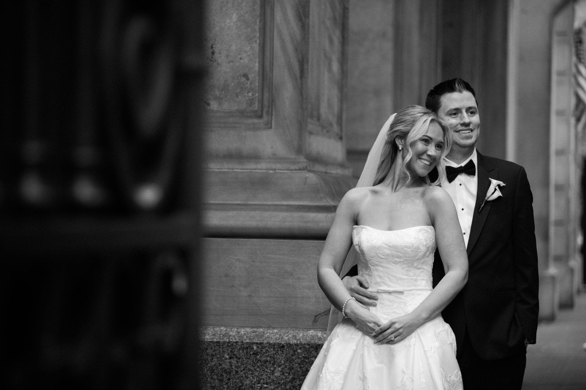 Black and white portrait of a bride and groom laughing against stone columns at a New Jersey wedding