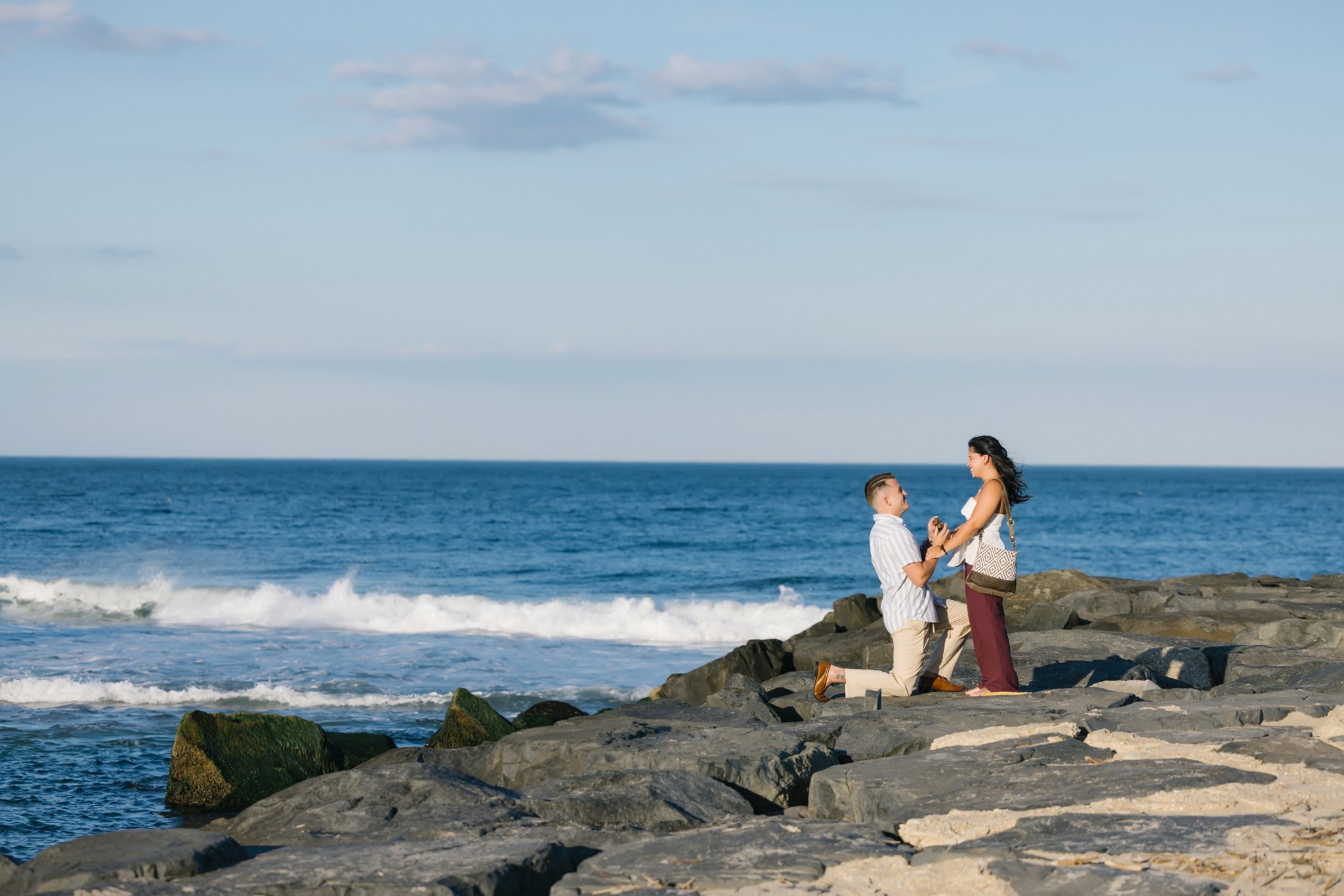 Man kneeling to propose on the jetty rocks in Asbury Park NJ
