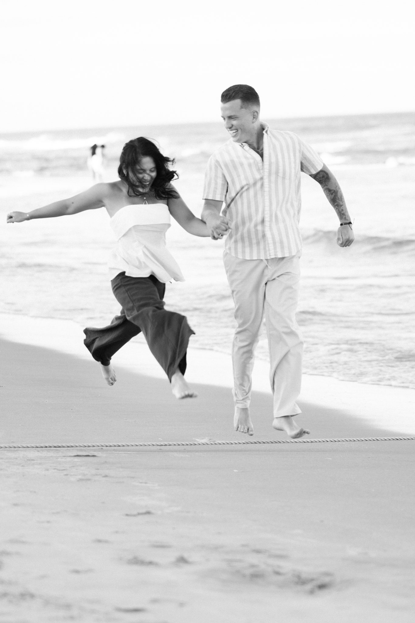 Black and white photograph of a newly engaged couple running on the Asbury Park beach