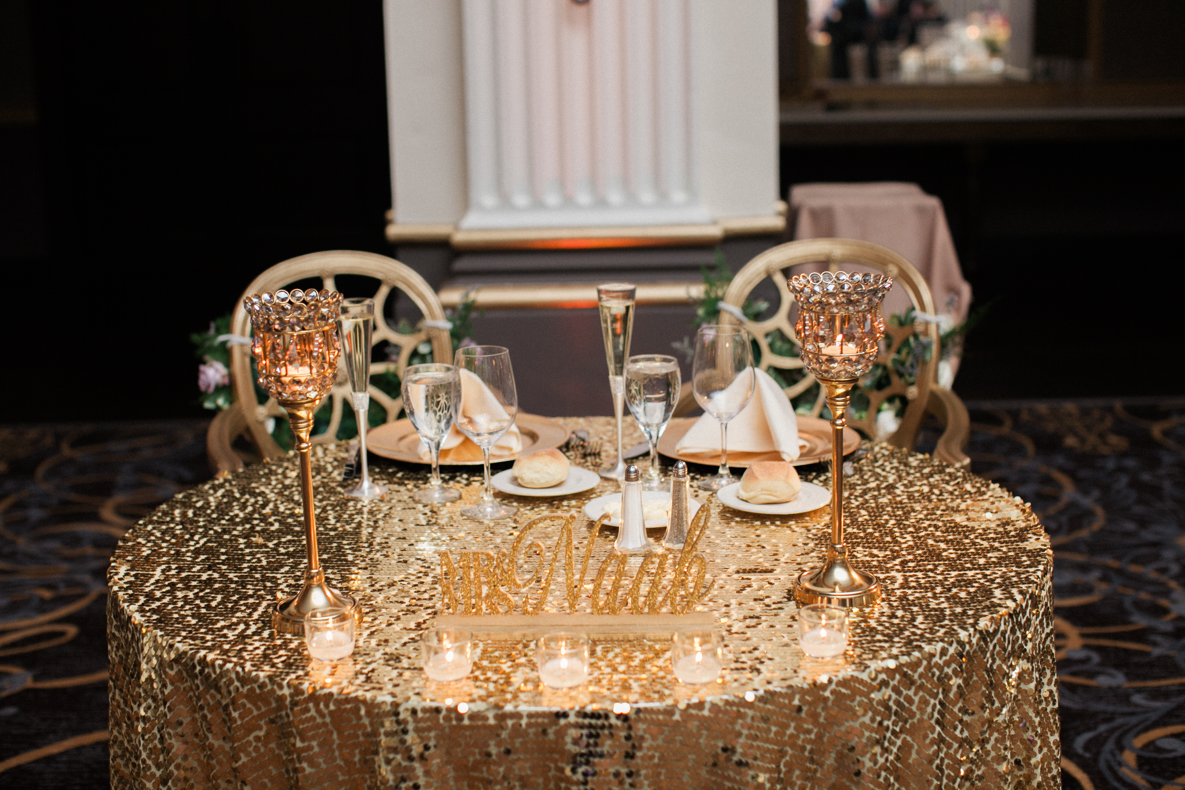 Sweetheart table at the Ballroom at the Ben in Philadelphia, set with gold sequin linen, crystal candle holders and a Mr and Mrs sign facing the dance floor, photographed by Jordan Brian