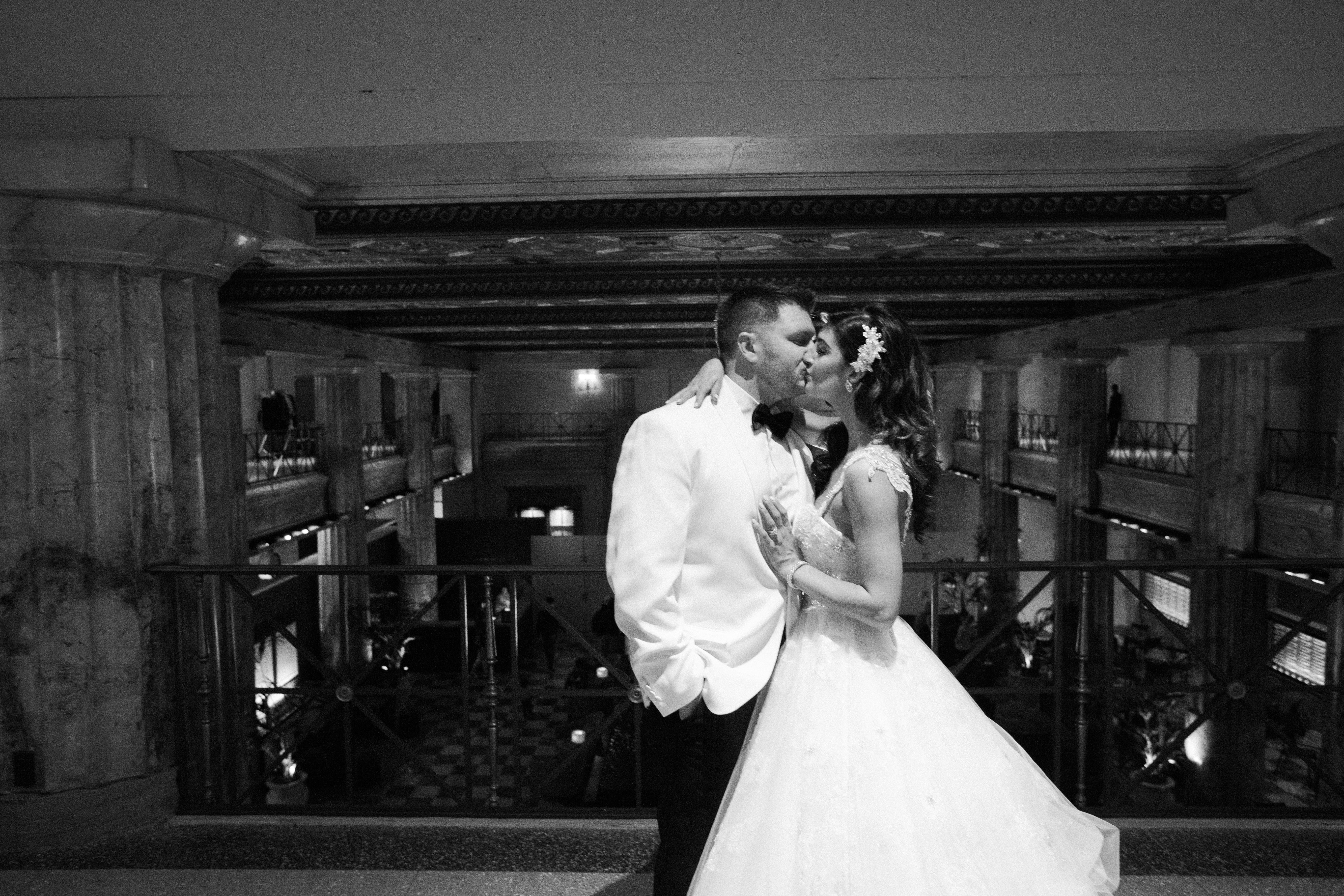 Bride and groom kissing on the wrap-around lobby mezzanine at Ballroom at the Ben, overlooking the room below