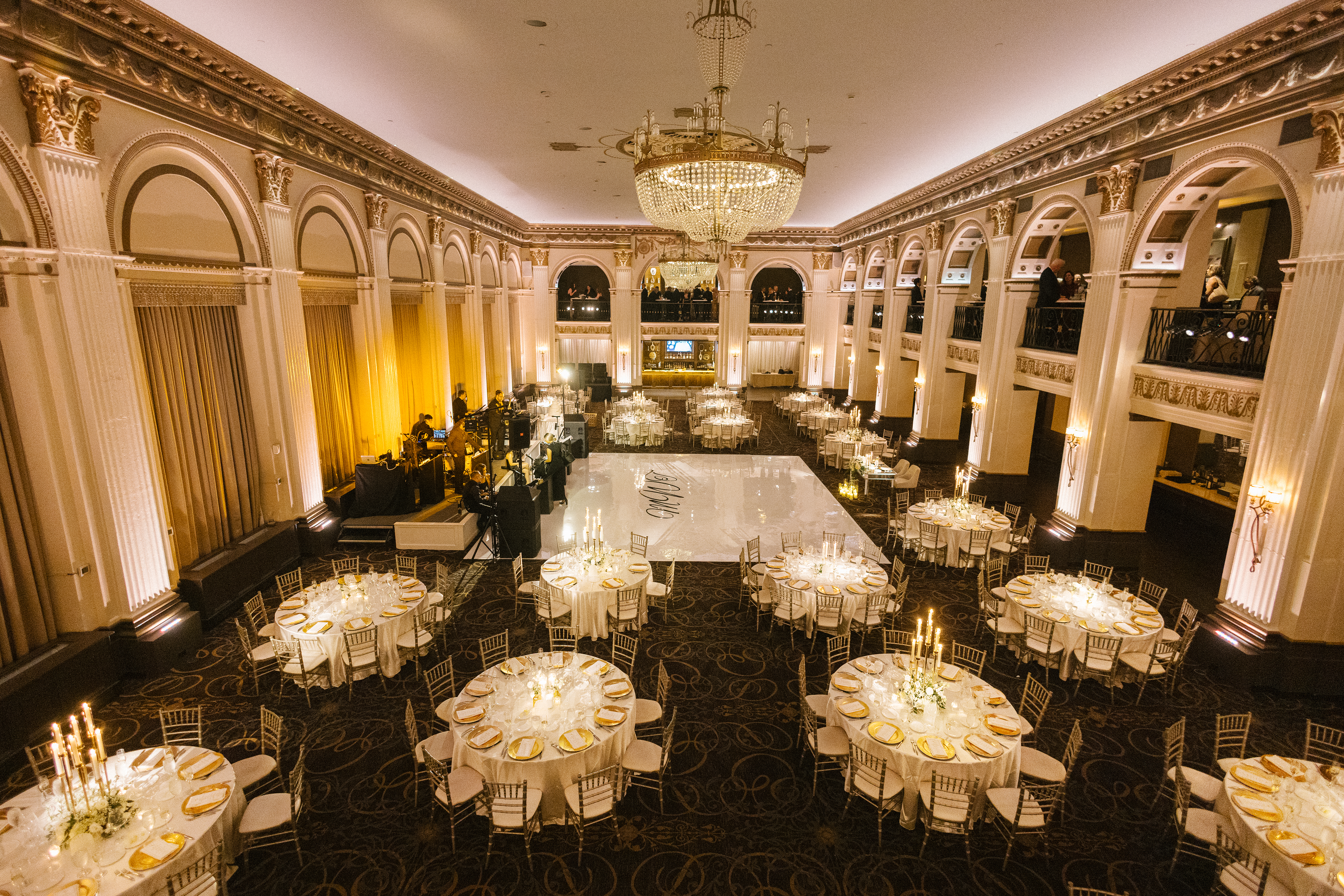 Reception layout at the Ballroom at the Ben in Philadelphia, viewed from the mezzanine with the white dance floor centered under the chandeliers, round tables and candlelight filling the room, photographed by Jordan Brian