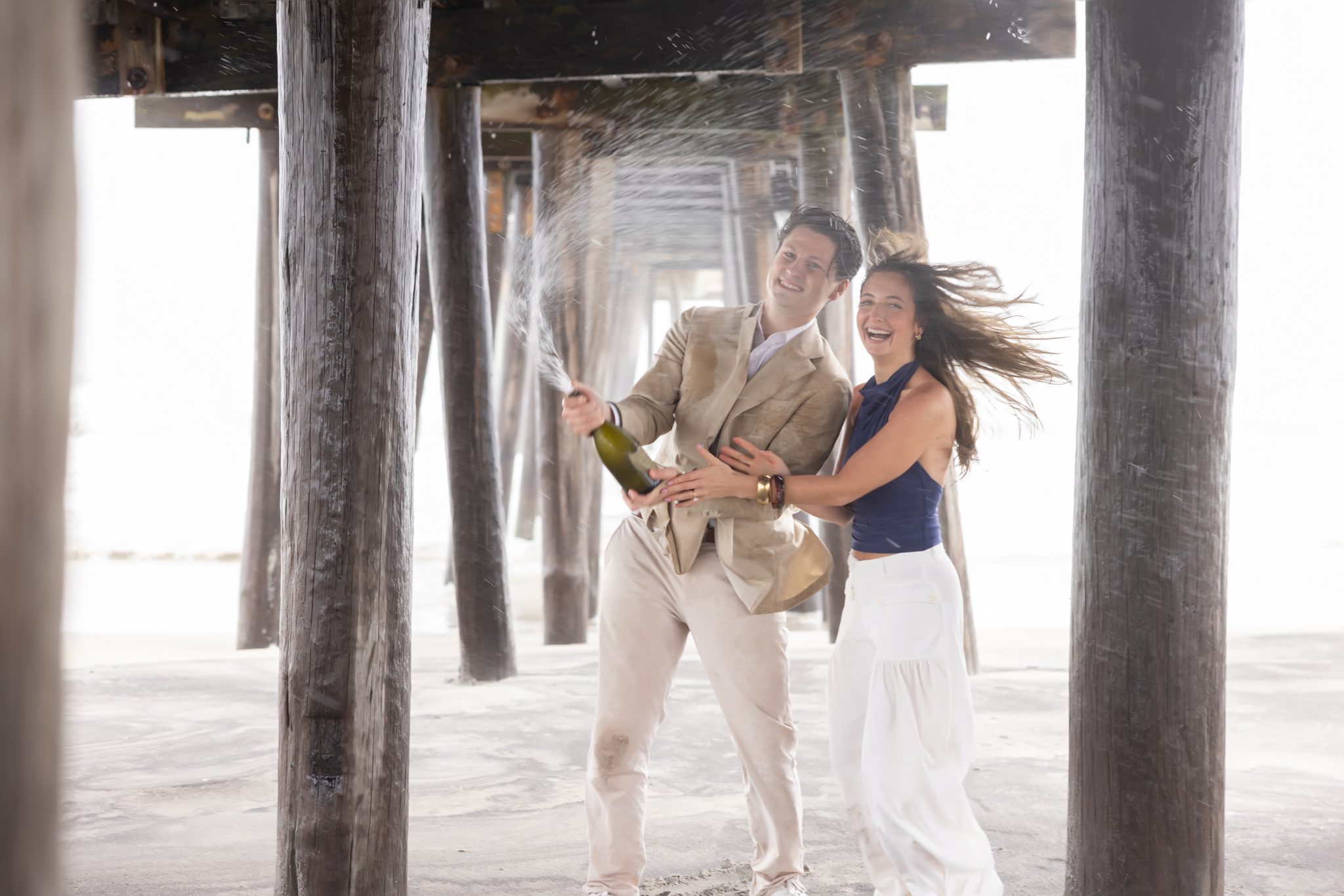 Couple walking with champagne on a windy Ocean City NJ beach after their proposal