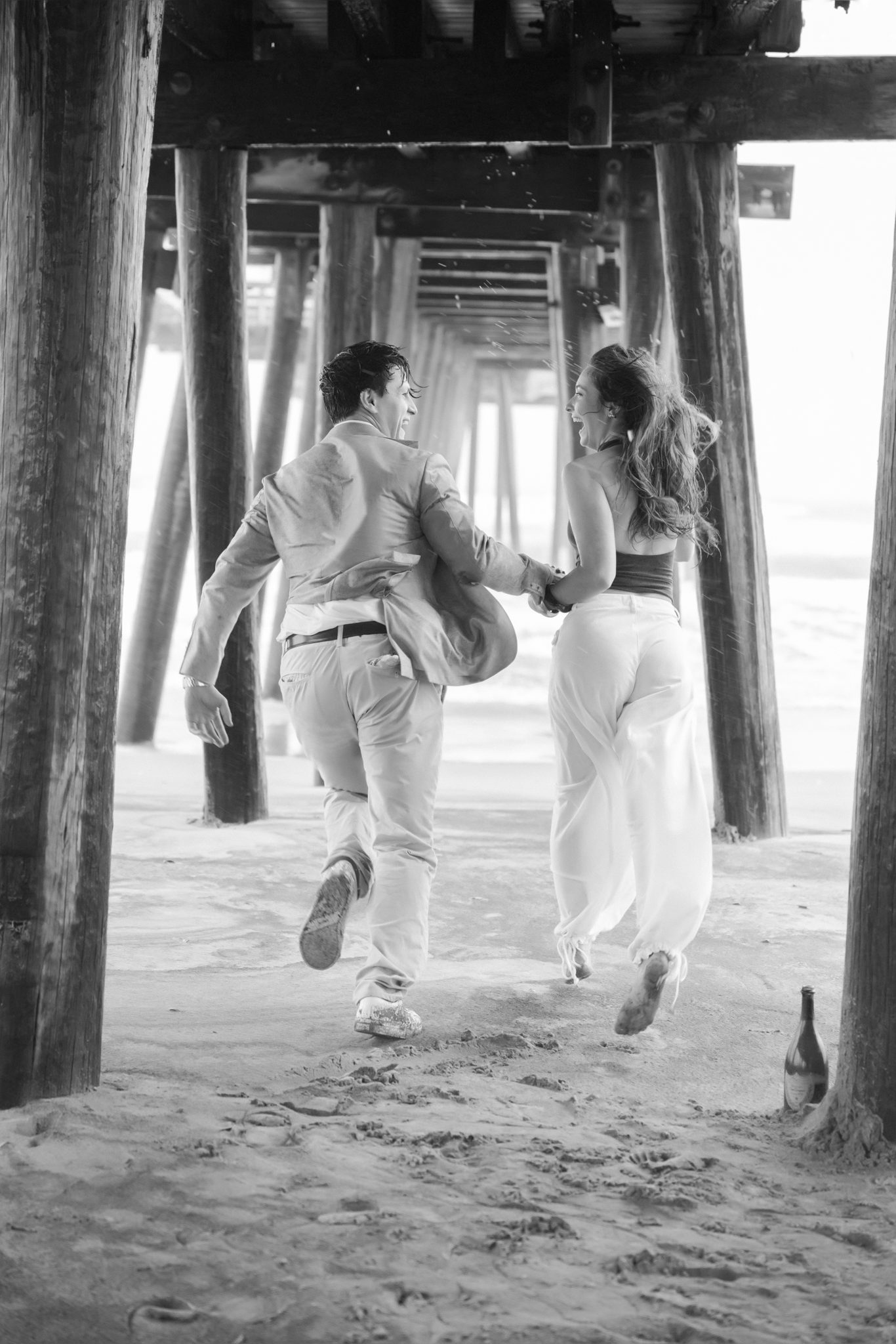 Newly engaged couple jumping with joy under the pier in Ocean City NJ