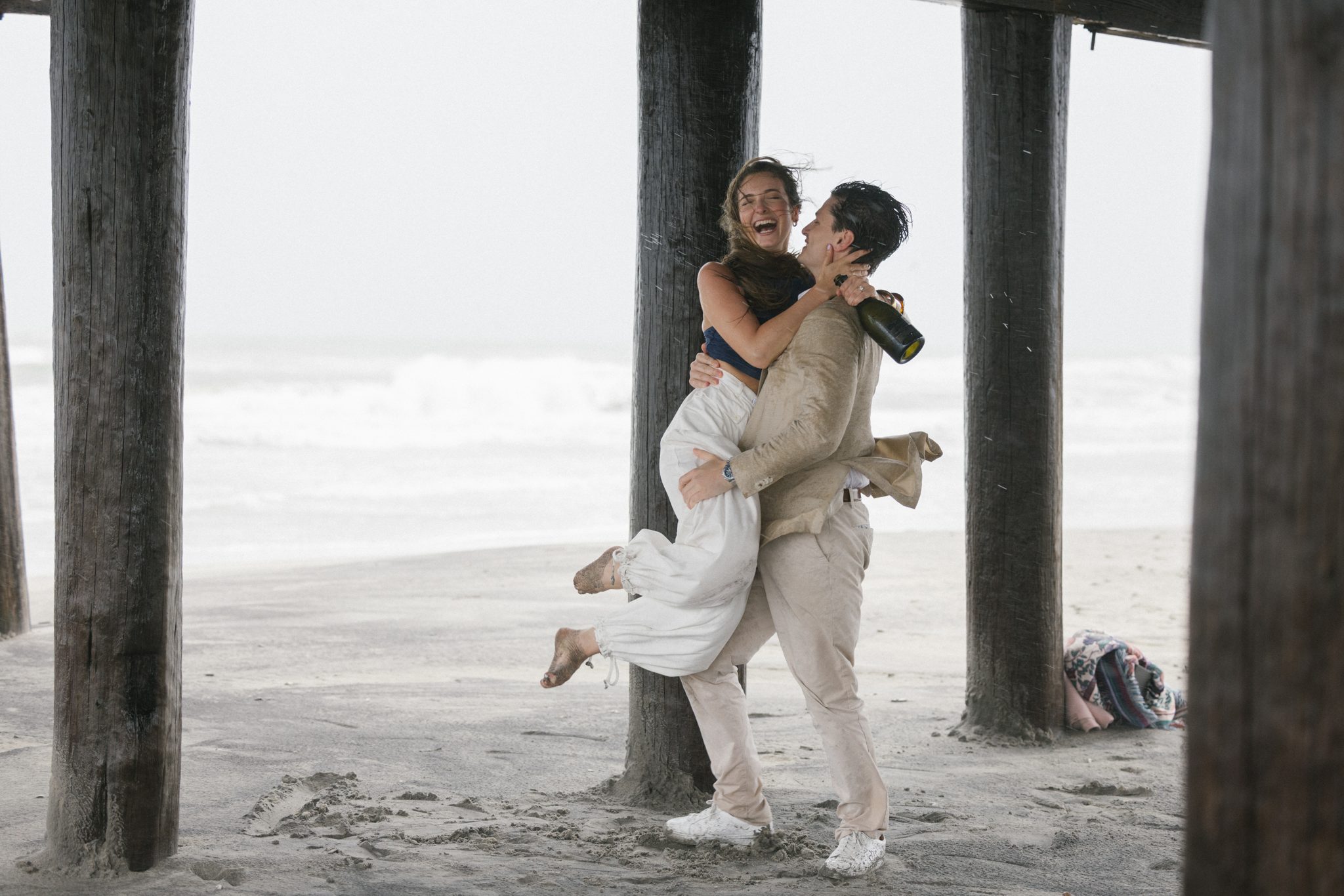 Groom to be lifting his fiancee laughing under the pier in Ocean City NJ
