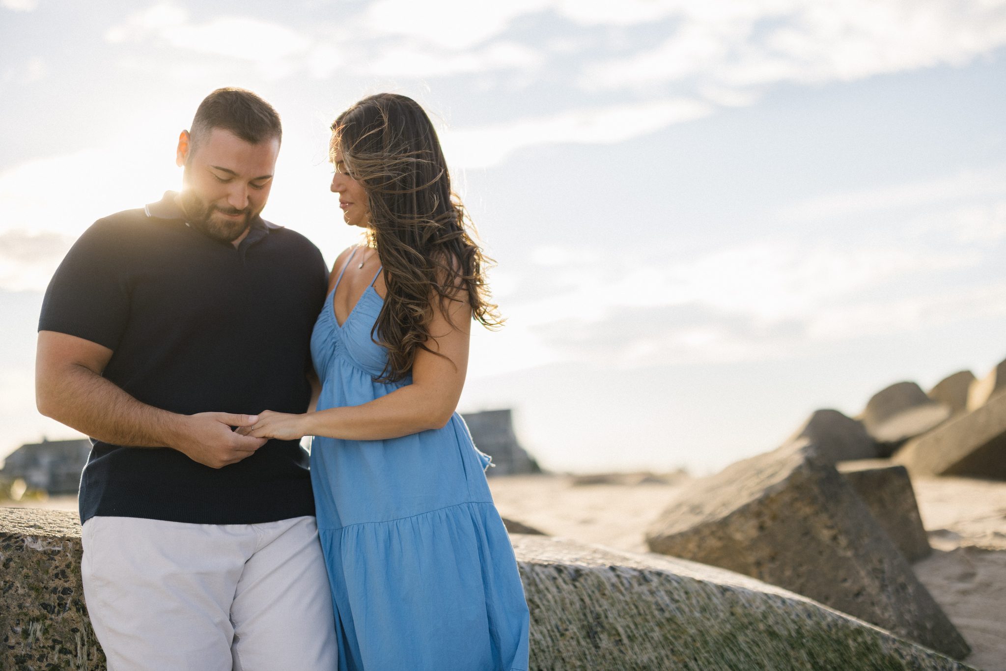 Newly engaged couple looking at the ring at golden hour on the Manasquan Inlet jetty in Point Pleasant Beach NJ