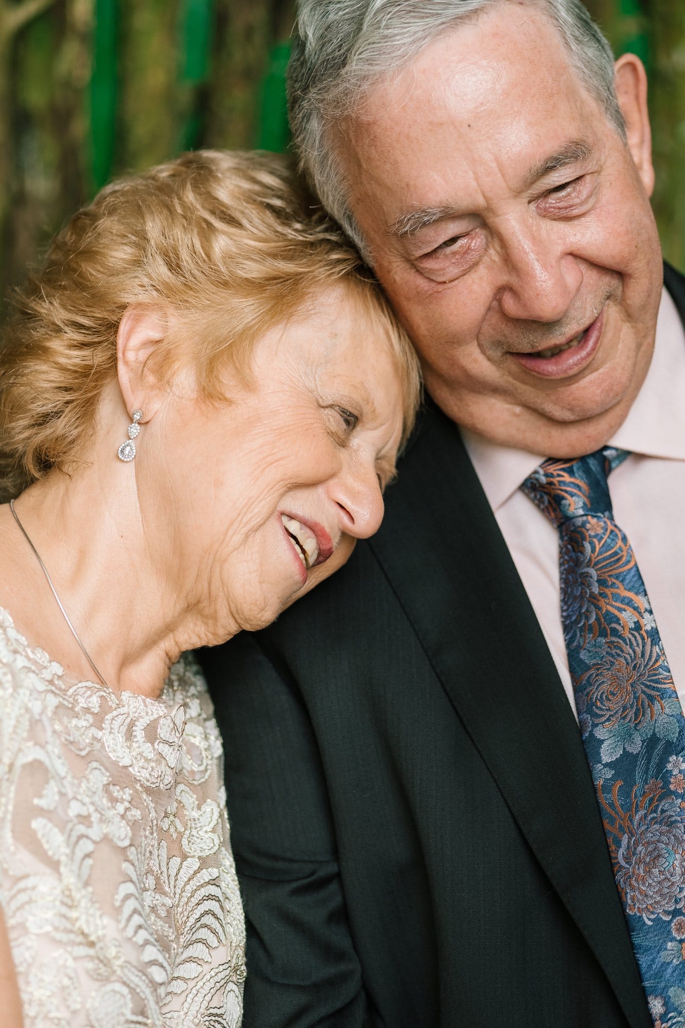 A wife laughing on her husband's shoulder at their 50th wedding anniversary in New Jersey